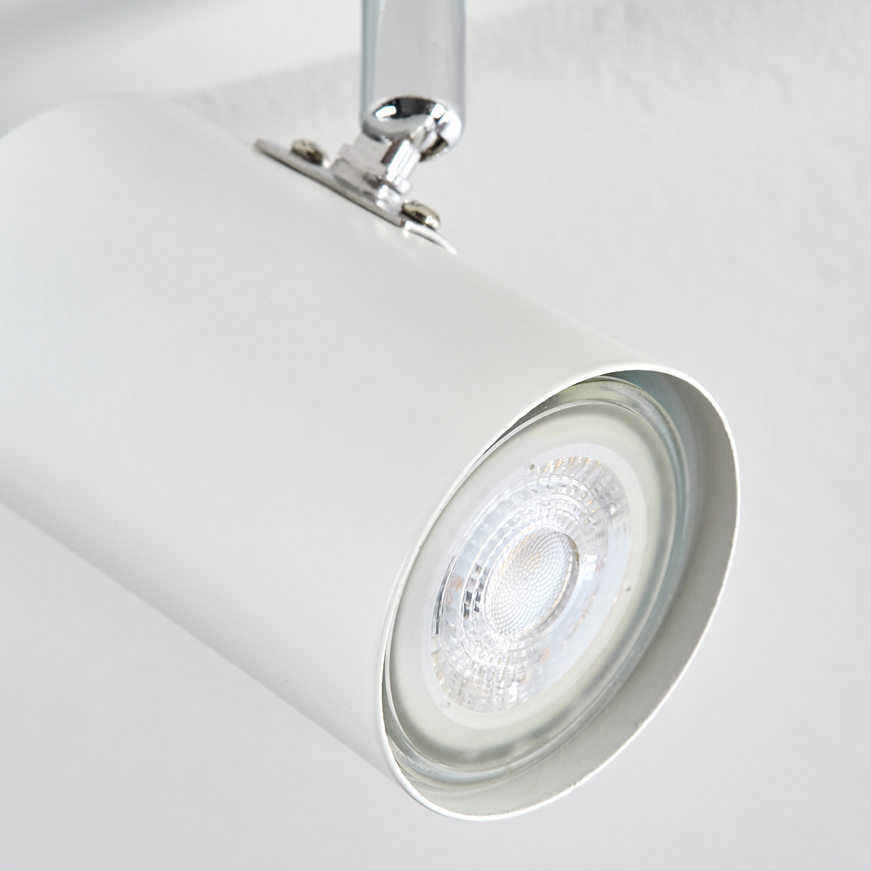 Ein weißer, zylindrischer Scheinwerfer ist an einer weißen Decke montiert. Das Licht hat eine silberne Halterung und eine helle LED-Lampe.