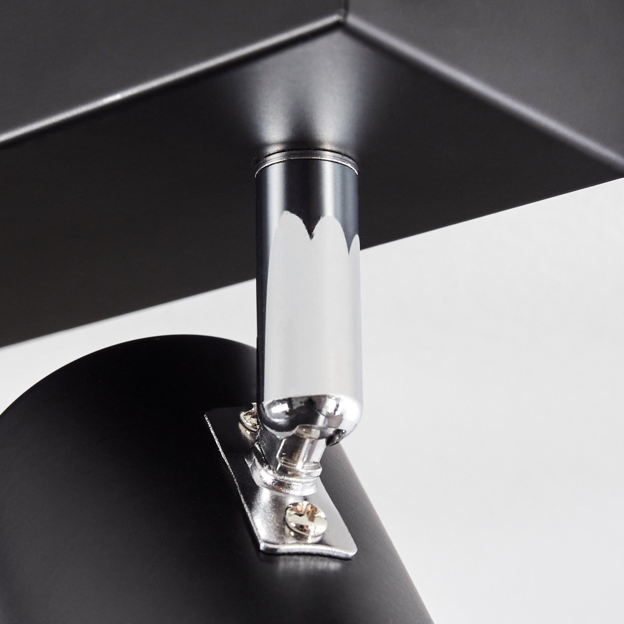 Nahaufnahme einer schwarzen Lampenhalterung mit Chromstütze. Die Lampe ist an einer weißen Wand befestigt. Die Deckenhalterung ist schwarz.