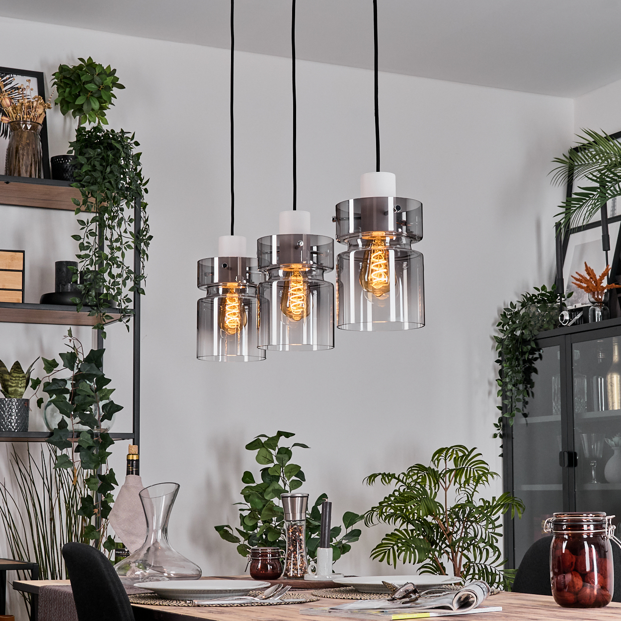 Esszimmer mit Hängelampen, Pflanzen und einem Holztisch mit Tellern, Gläsern und Essen.