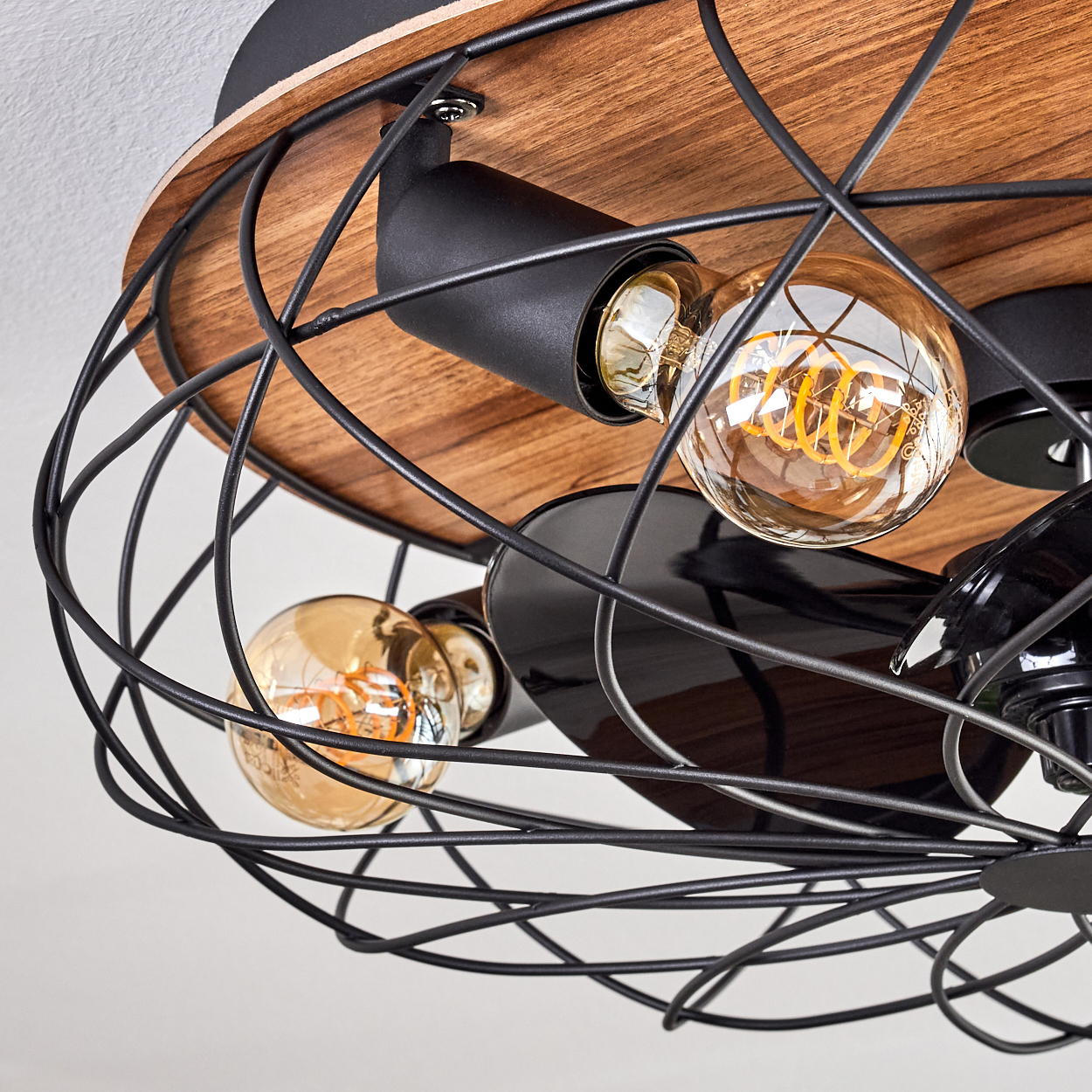 Nahaufnahme einer Deckenleuchte. Sie hat drei Edison-Glühbirnen in einem schwarzen Metallkäfig, montiert auf Holz und schwarzem Metall.