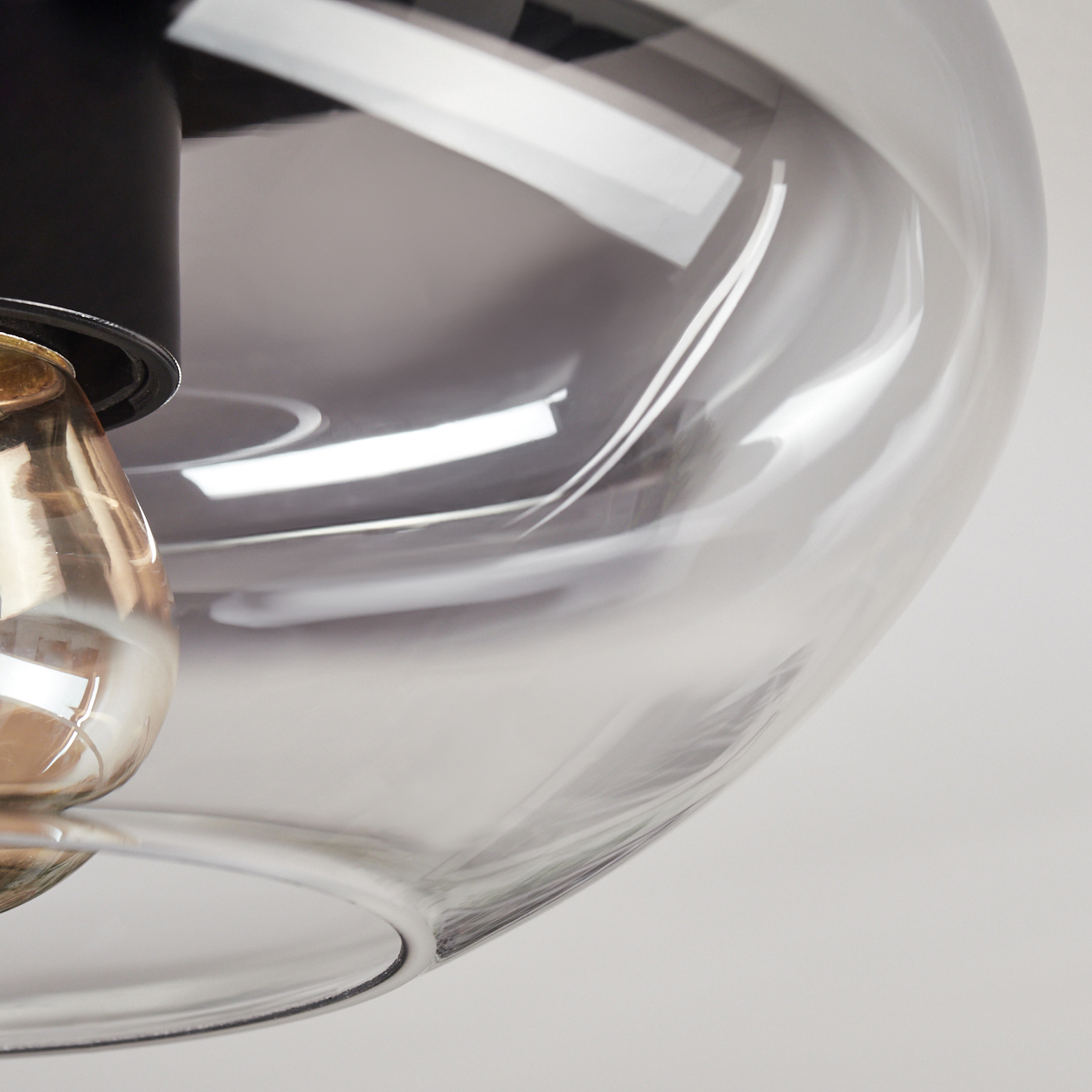 Nahaufnahme einer Glasleuchte. Sie hat einen schwarzen Deckel, einen transparenten Glasschirm und eine sichtbare Glühbirne.