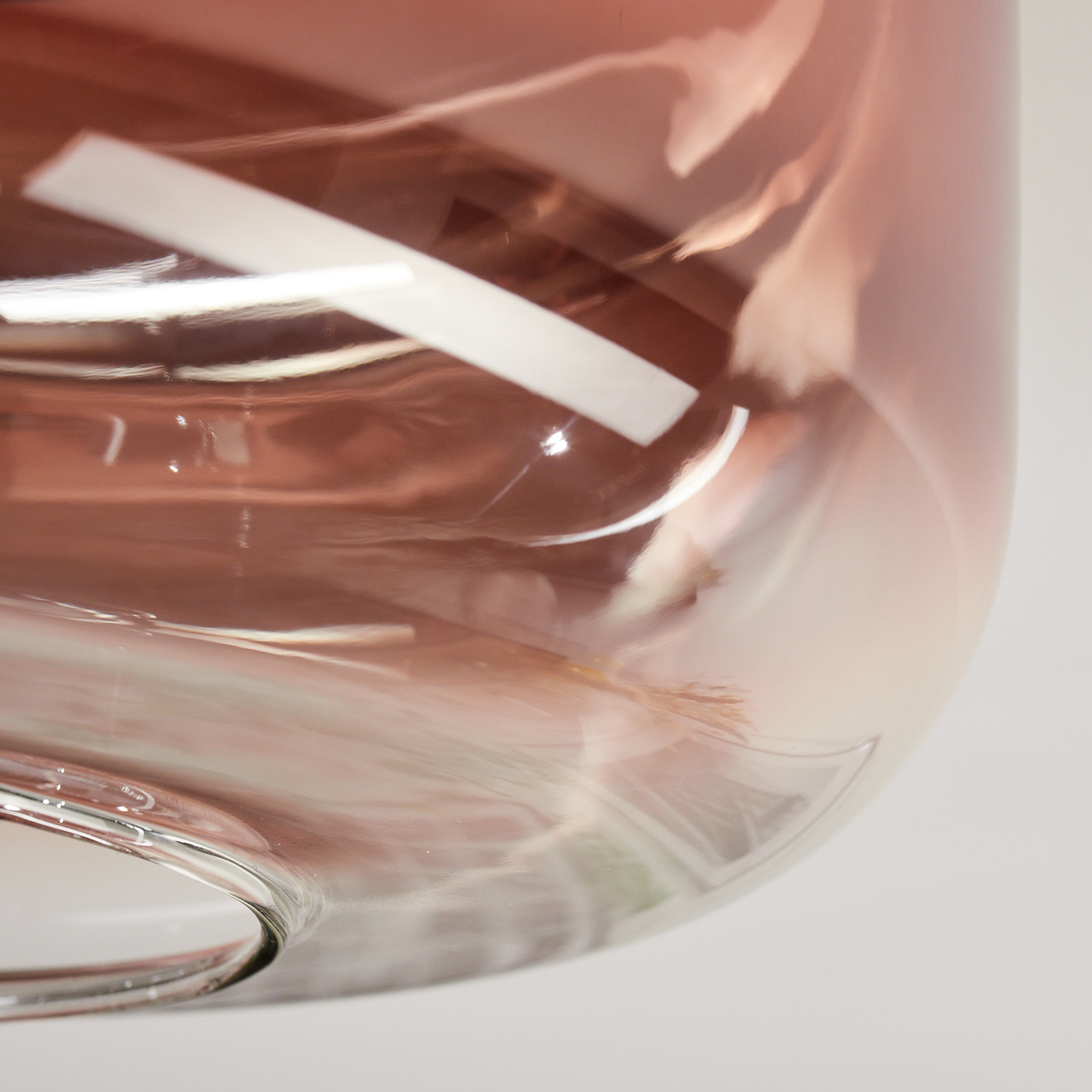 Nahaufnahme eines Glasbehälters mit zartrosa Farbton und weißem Etikett. Das Glas reflektiert Licht und erzeugt unscharfe Muster.
