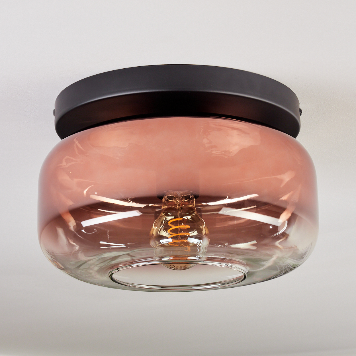 Moderne Deckenleuchte mit Glasschirm und schwarzem Sockel. Das Glas ist rosa, und die Glühbirne ist sichtbar.
