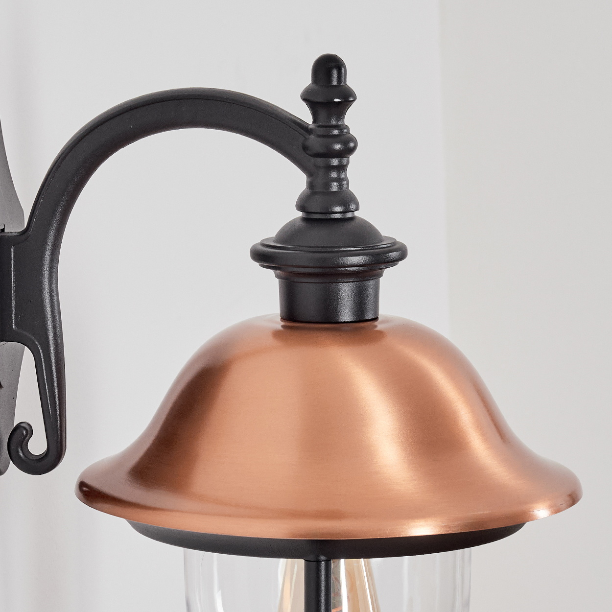 Nahaufnahme eines kupferfarbenen Lampenschirms mit schwarzem Metallrahmen. Unter dem Schirm ist eine klare Glühbirne zu sehen.