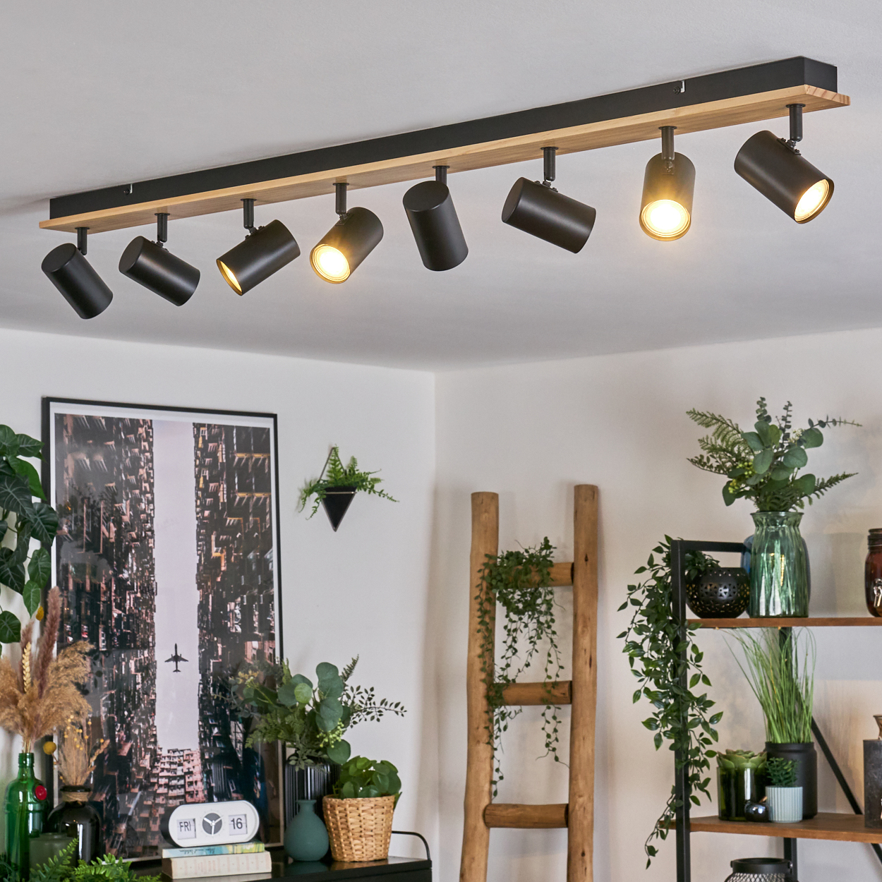 Ein modernes Zimmer mit einer Deckenleuchte. Das Zimmer hat ein Bild an der Wand, Pflanzen und eine Holzleiter.