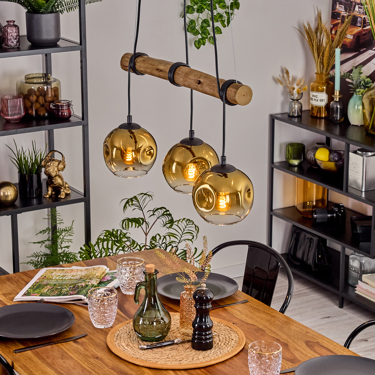 Esstisch mit drei goldenen Pendelleuchten. Tisch mit Tellern, Gläsern und Dekoration. Regale mit Vasen und Dekorationsartikeln.