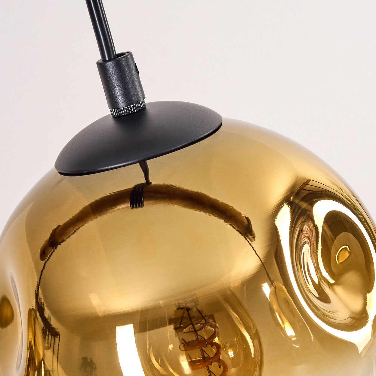 Nahaufnahme einer modernen Lampe mit goldenem Glasschirm. Die Glühbirne ist sichtbar. Die Lampe wird von einem schwarzen Kabel gehalten.