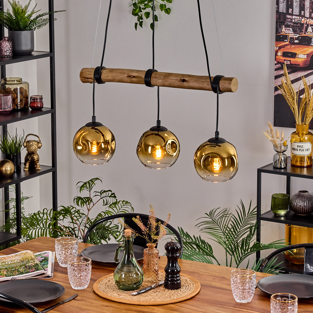 Esszimmer mit Holztisch, drei hängenden Goldlampen, Pflanzen und Geschirr. Regale auf beiden Seiten. Ein Gemälde im Hintergrund.