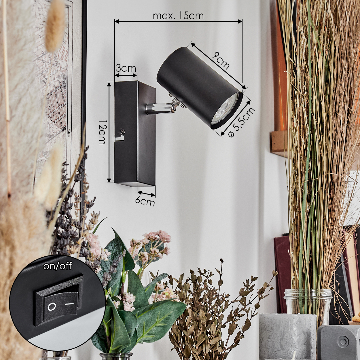 Eine schwarze Wandleuchte ist an einer weißen Wand montiert. Die Lampe befindet sich neben Blumen und hohem Gras. Ein Ein/Aus-Schalter ist sichtbar.