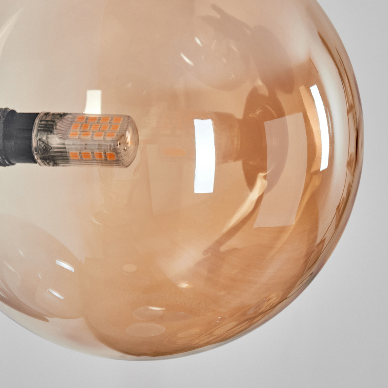 Nahaufnahme einer großen, bernsteinfarbenen Glühbirne. Die Oberfläche reflektiert Licht. Ein kleines, klares LED-Element ist sichtbar.