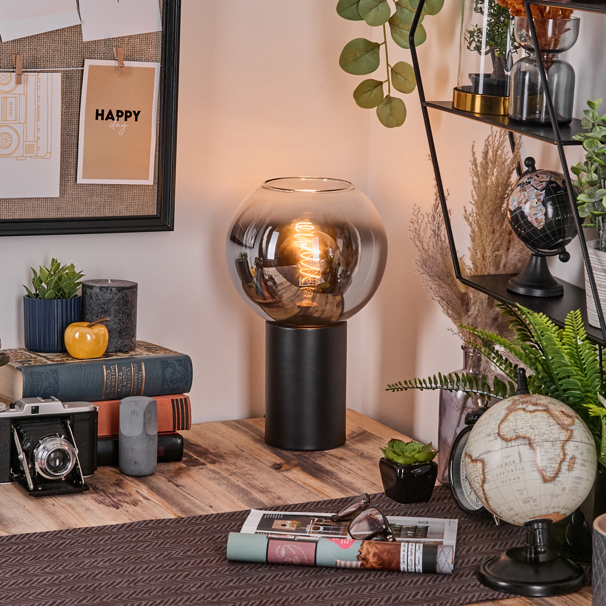 Ein Schreibtisch mit Lampe, Büchern, Kamera und Globus. Pflanzen und andere Dekorationsartikel sind ebenfalls vorhanden.