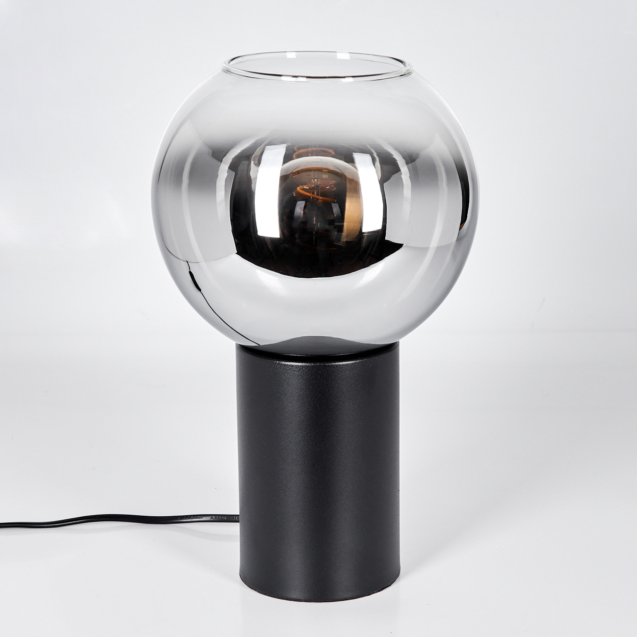 Eine moderne Lampe mit kugelförmigem Glasschirm, Chromausführung und schwarzem Sockel. Im Schirm ist eine Glühbirne sichtbar.