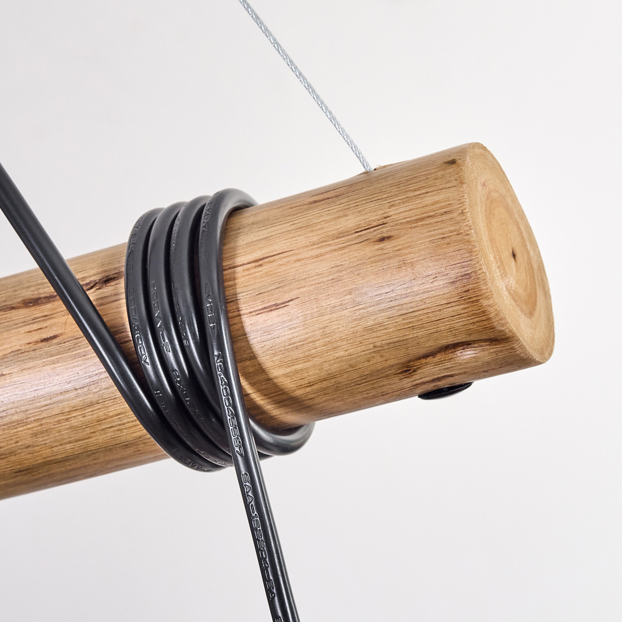 Holzstamm mit schwarzem Kabel umwickelt. Ein Silberdraht hängt von oben. Der Hintergrund ist weiß.