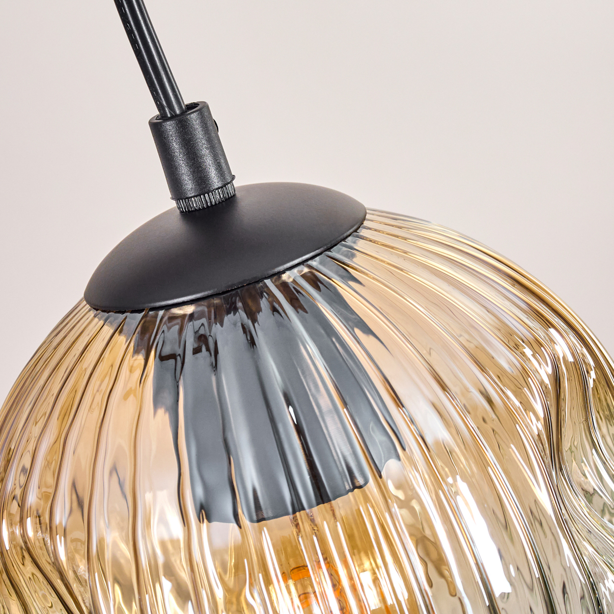 Nahaufnahme eines Glasschirms. Der Schirm ist bernsteinfarben und hat eine gerippte Textur. Eine schwarze Metallkappe und ein Kabel sind sichtbar.