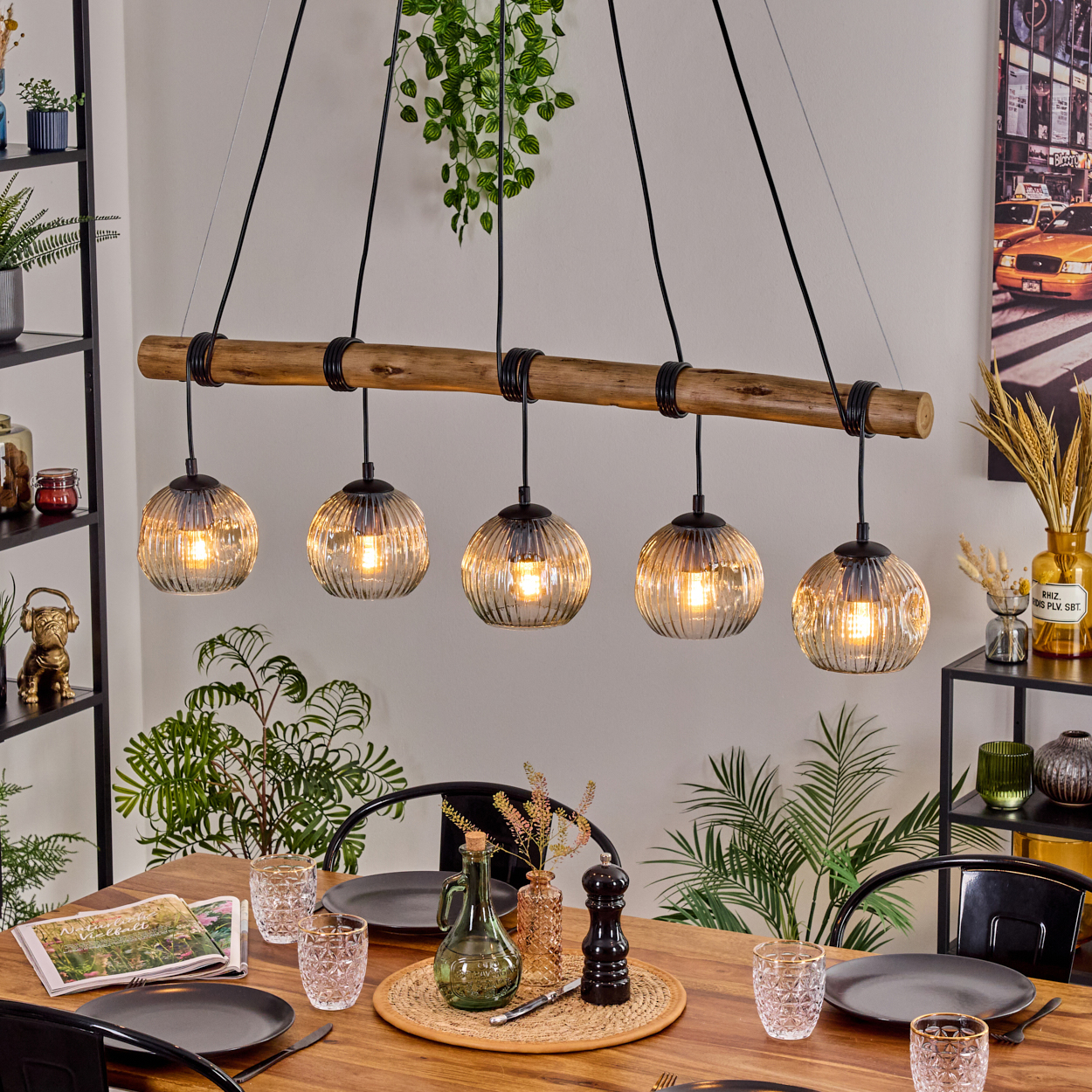Esszimmer mit Holztisch, schwarzen Stühlen und einem Kronleuchter mit fünf Kugelleuchten. Pflanzen und Dekorationen sind ebenfalls sichtbar.