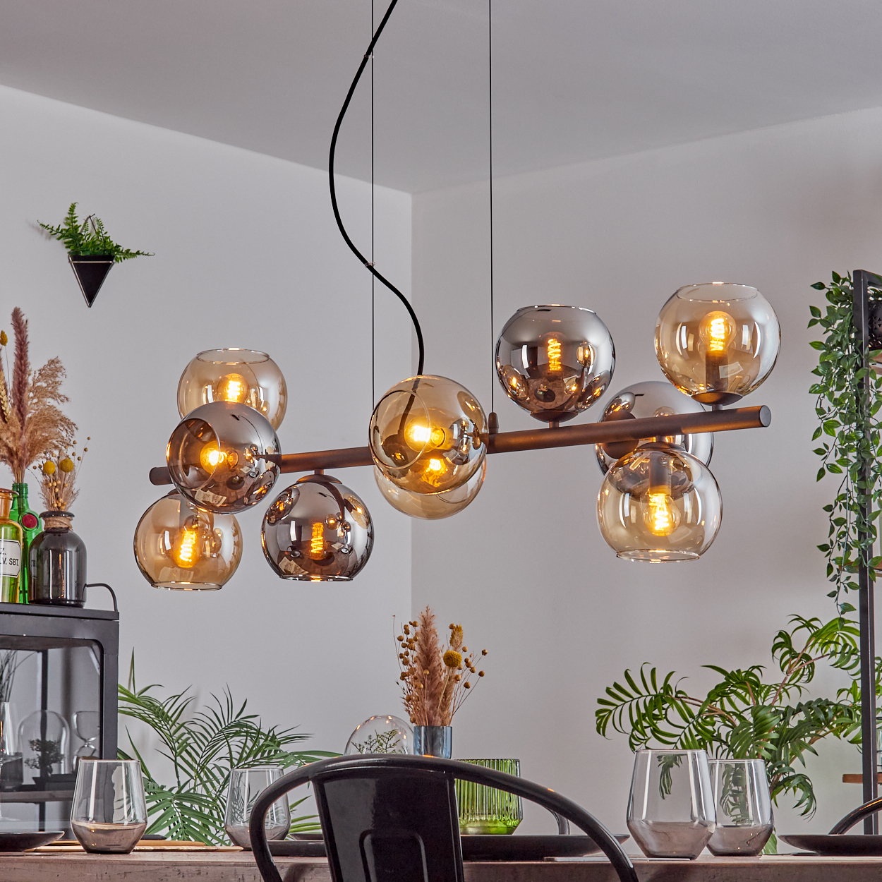 Ein modernes Esszimmer mit einem Kronleuchter mit kugelförmigen Glaskolben. Pflanzen und Gläser stehen auf dem Tisch.