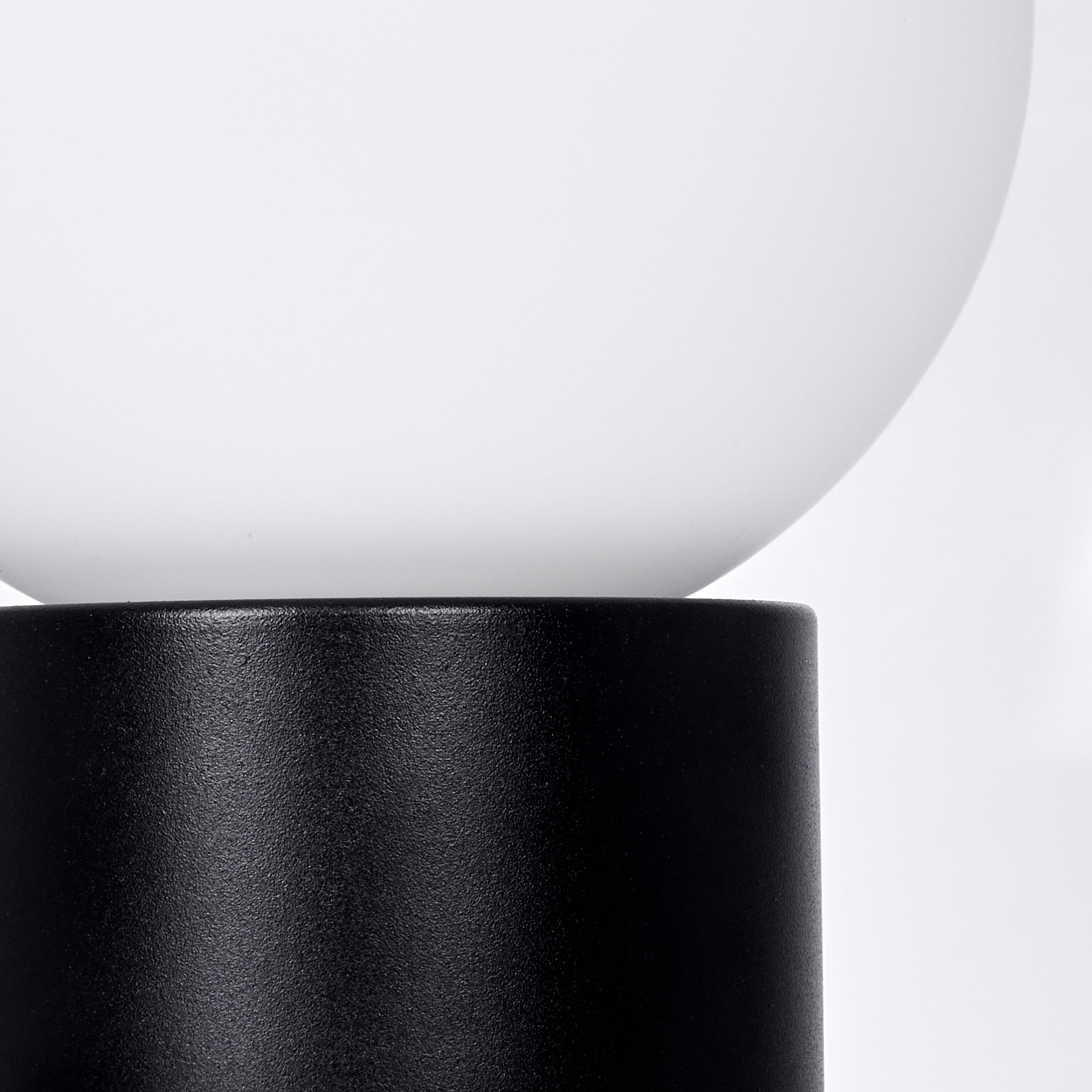 Nahaufnahme einer Lampe mit schwarzem zylindrischen Sockel und weißem, kugelförmigem Schirm. Der Hintergrund ist weiß.