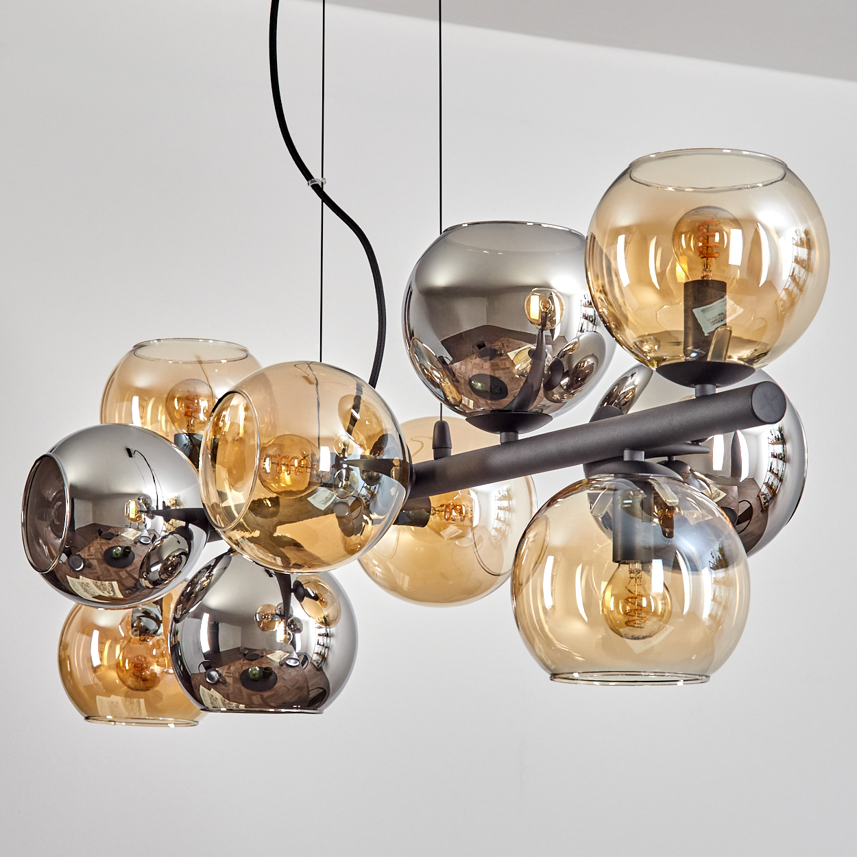 Eine moderne Deckenleuchte mit mehreren kugelförmigen Glasschirmen in Bernstein und Silber, jede mit einer Glühbirne, auf einem dunklen Metallrahmen.