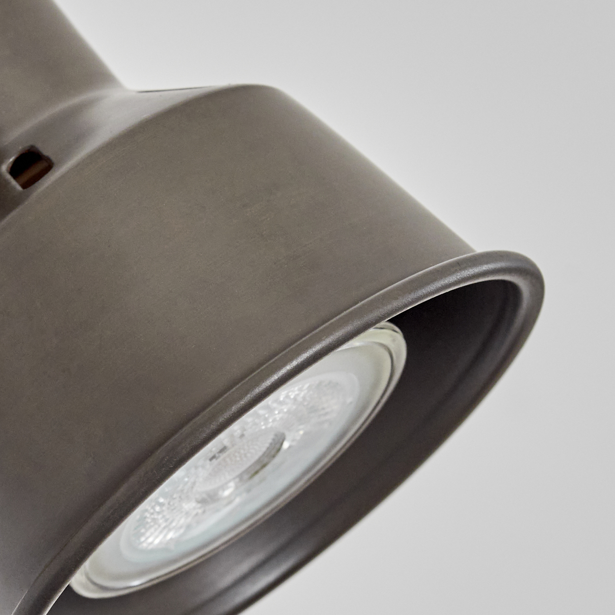 Nahaufnahme einer dunkelgrauen Lampe. Die Lampe hat einen zylindrischen Schirm mit einer am Ende sichtbaren Glühbirne. Der Hintergrund ist weiß.