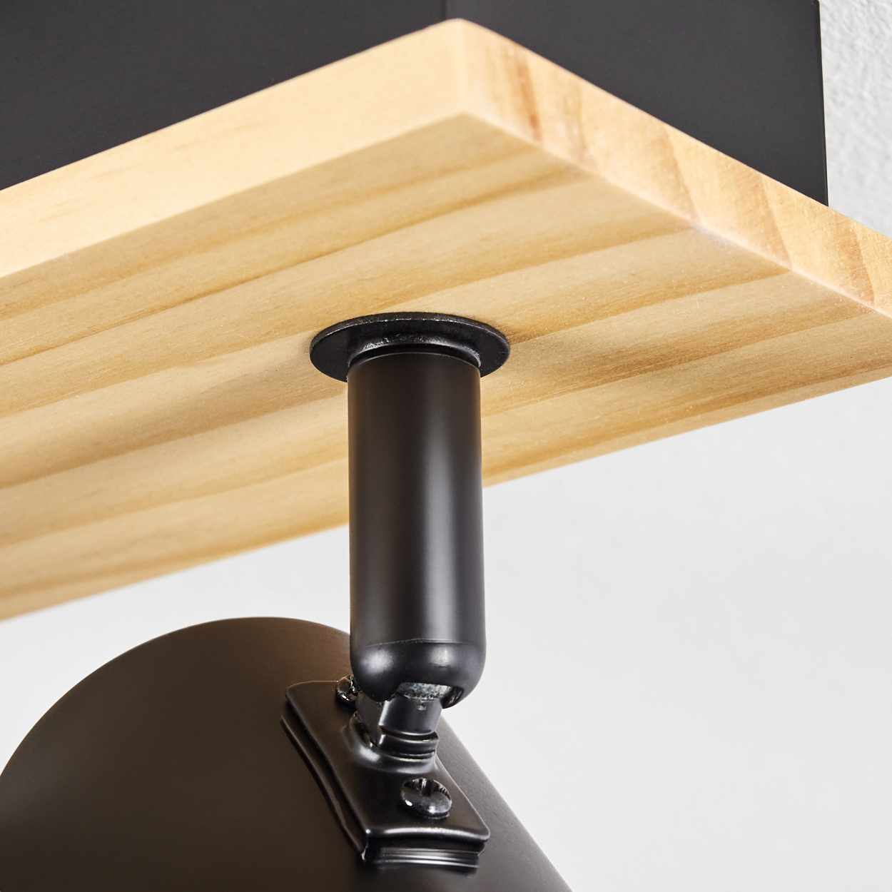 Nahaufnahme einer schwarzen Lampenhalterung, die an einem Holzregal befestigt ist. Das Regal ist helles Holz. Der Hintergrund ist weiß.