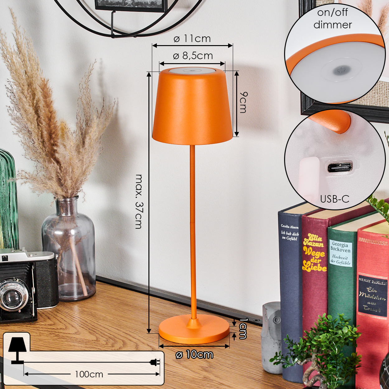 Eine orangefarbene Lampe steht auf einem Holztisch mit Büchern, einer Vase mit Pampasgras und einer Kamera, Maße sind angegeben.