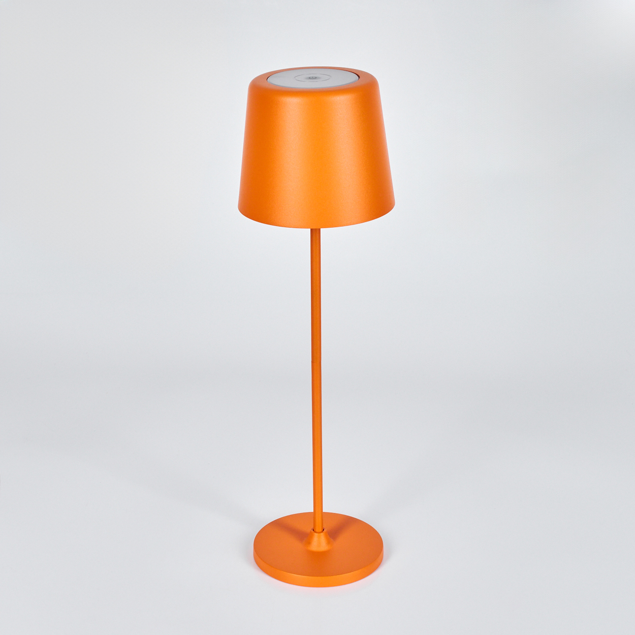 Eine orangefarbene Lampe auf weißem Hintergrund. Sie hat einen runden Fuß, einen dünnen Stiel und einen Lampenschirm, der oben breiter ist.