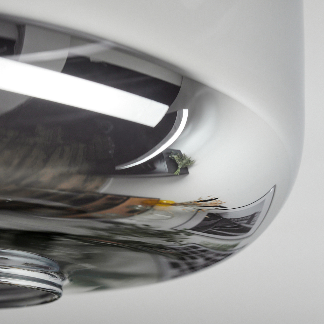 Nahaufnahme eines glänzenden, metallischen Objekts, das eine Szene mit einer kleinen Pflanze und Bildern reflektiert. Das Objekt ist gebogen und glatt.