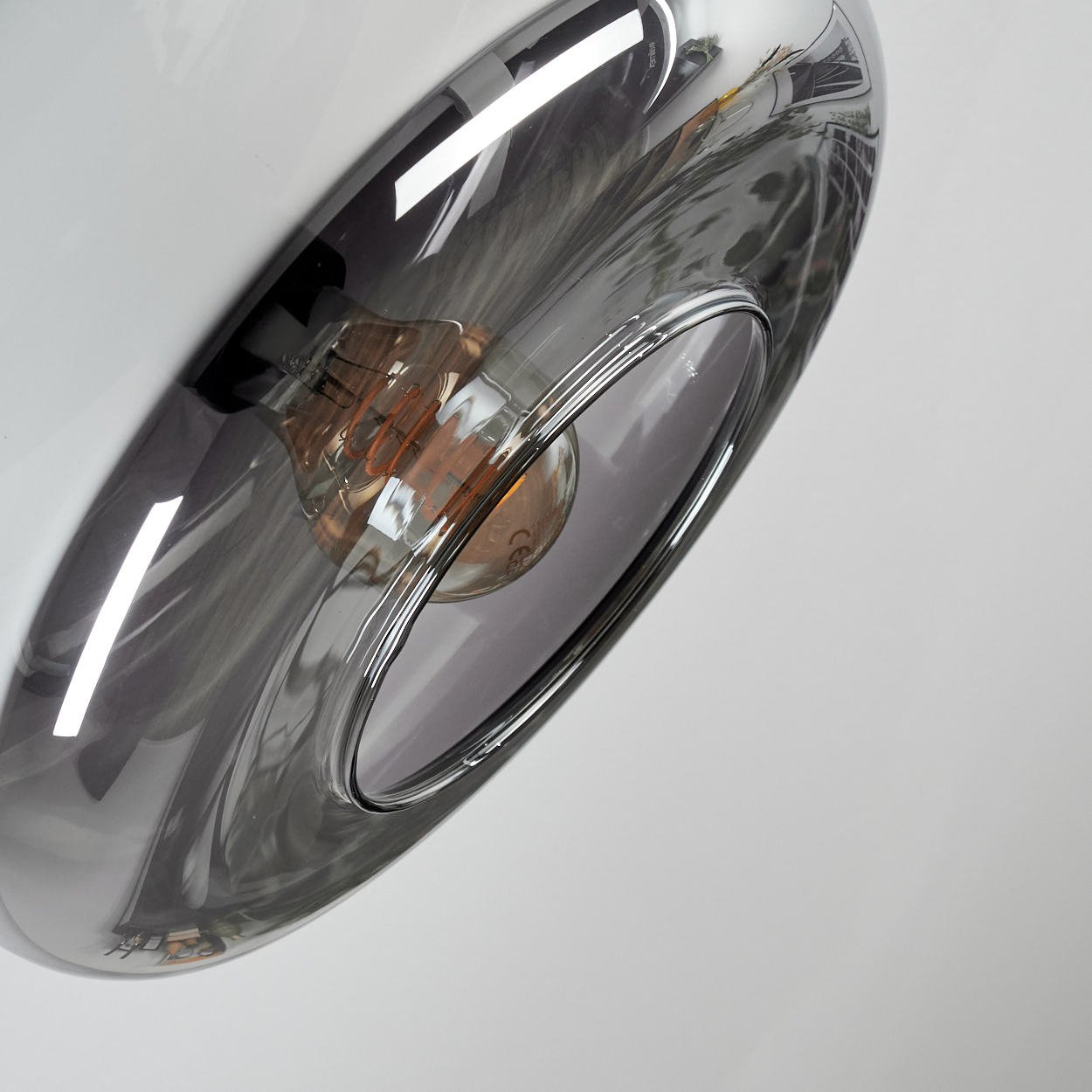 Nahaufnahme einer modernen Lampe mit reflektierendem, grauem Glasschirm. Im Inneren ist eine orangefarbene Glühbirne zu sehen.