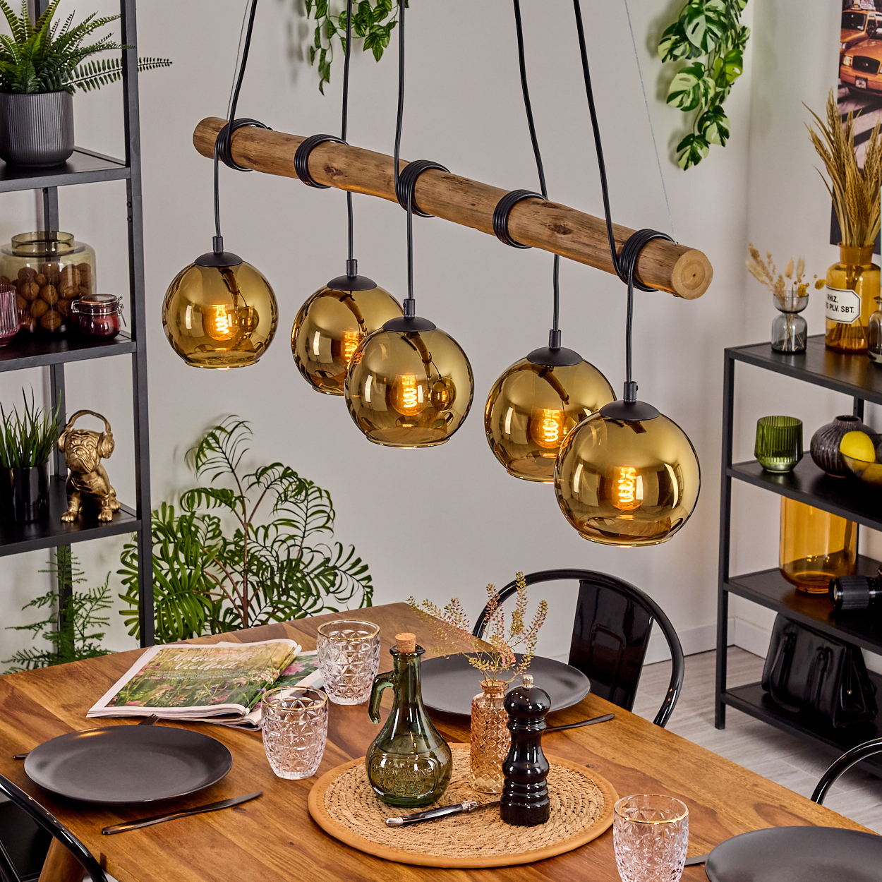 Esszimmer mit Holztisch, sechs goldenen Hängelampen und Dekoration. Pflanzen und Regale im Hintergrund.