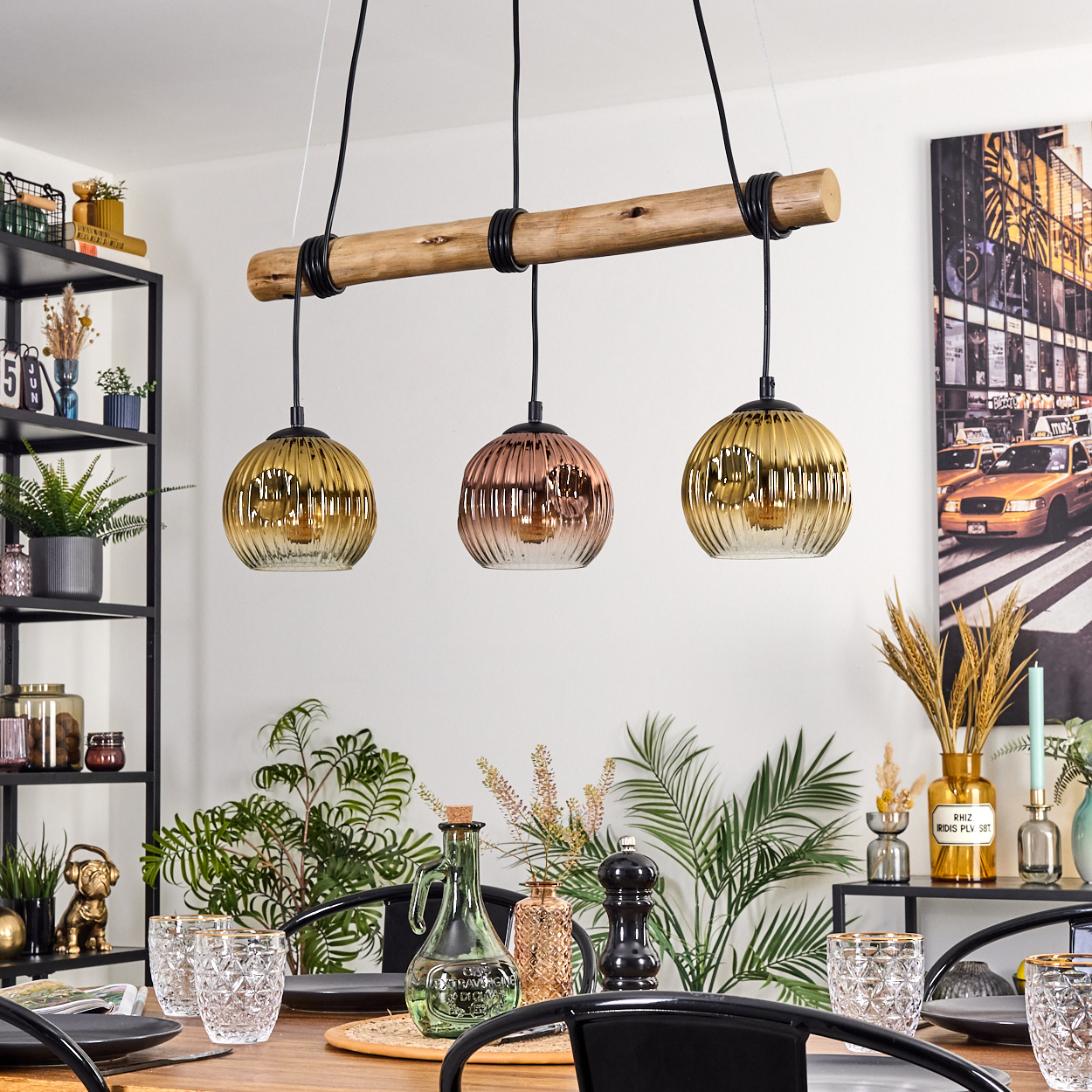 Esszimmer mit Holztisch, drei Pendelleuchten und verschiedenen Dekorationen, darunter Pflanzen und Gläser.