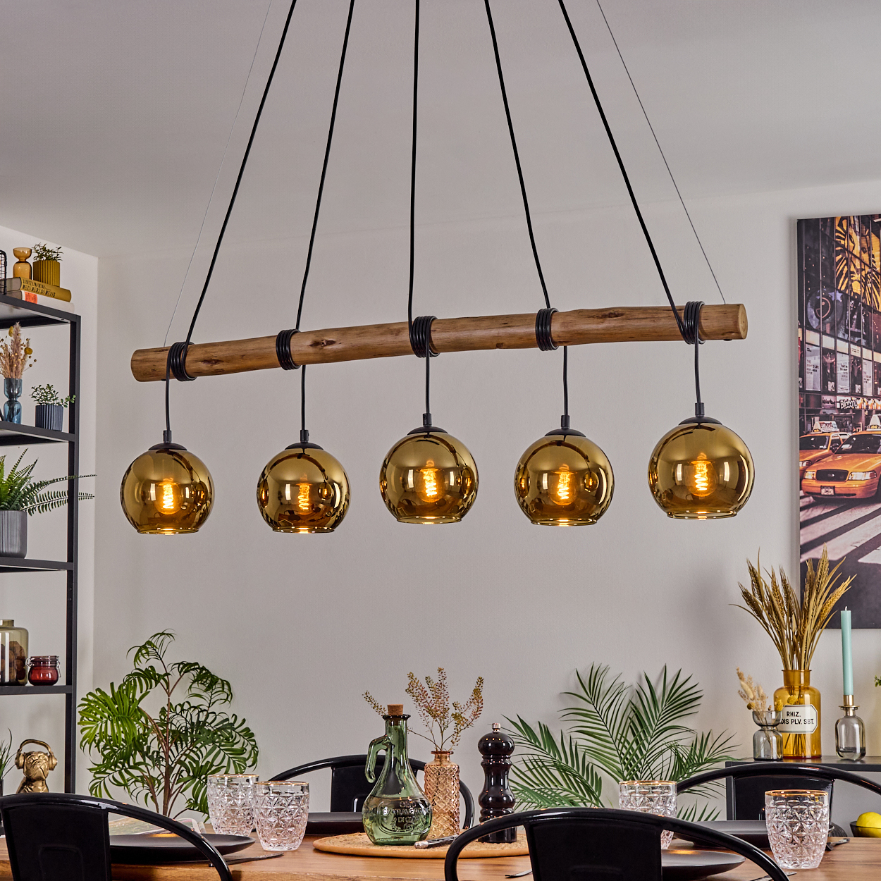 Ein Esszimmer mit Holztisch, schwarzen Stühlen und Kronleuchter mit goldenen Kugellampen. Pflanzen und Dekoration sind ebenfalls sichtbar.