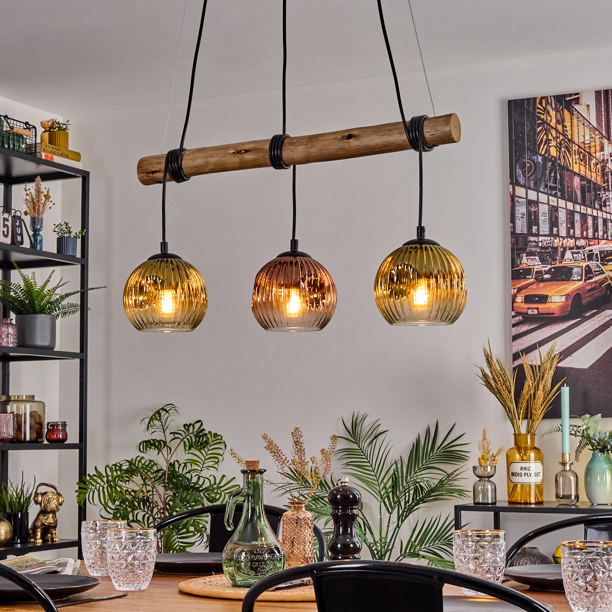 Drei Pendelleuchten hängen über einem Tisch. Die Leuchten sind gold- und kupferfarben. Ein Tisch ist mit Gläsern und Pflanzen gedeckt.