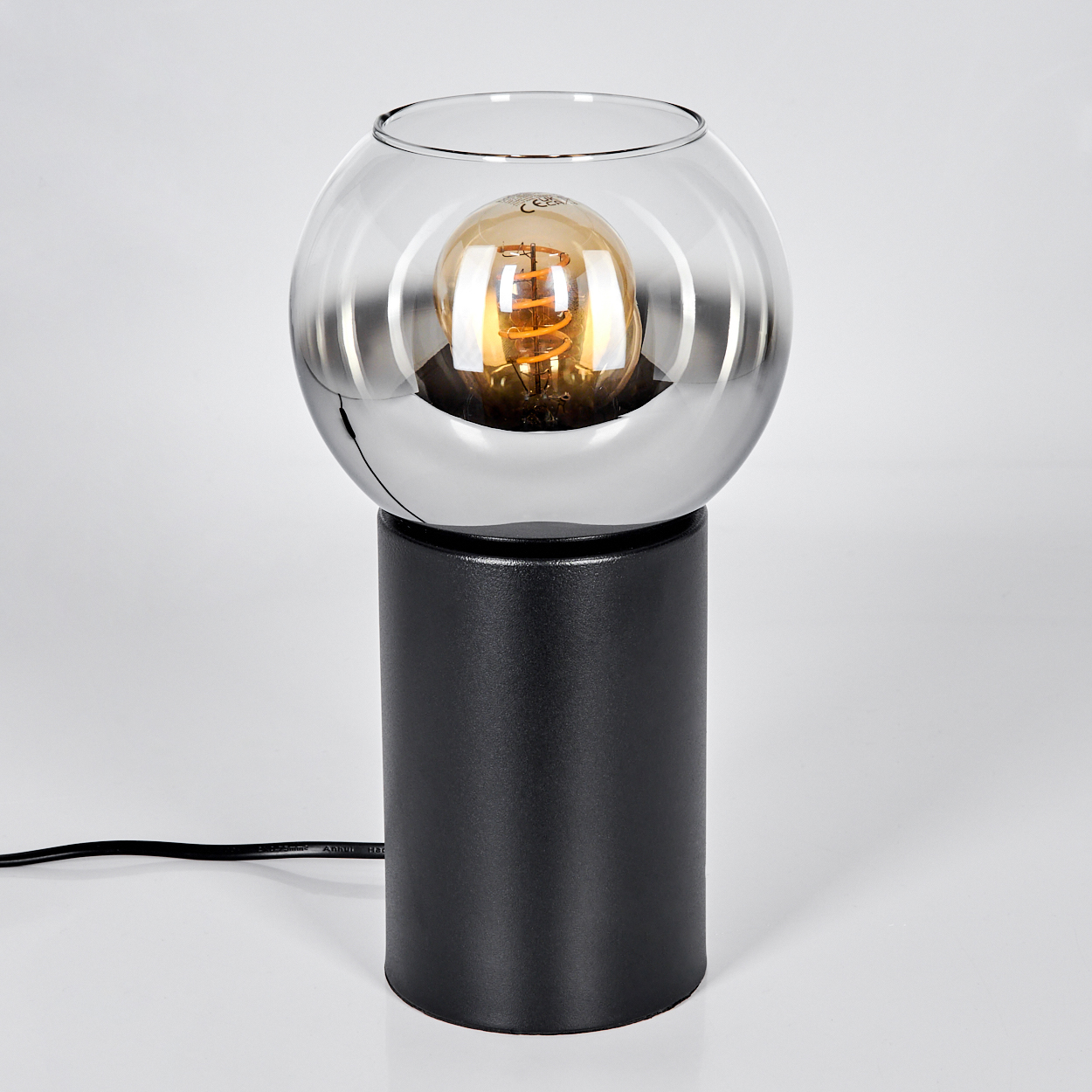 Eine moderne Lampe mit schwarzem Sockel, verchromtem Mittelteil und Glaskugel mit leuchtender, orangefarbener Glühbirne.