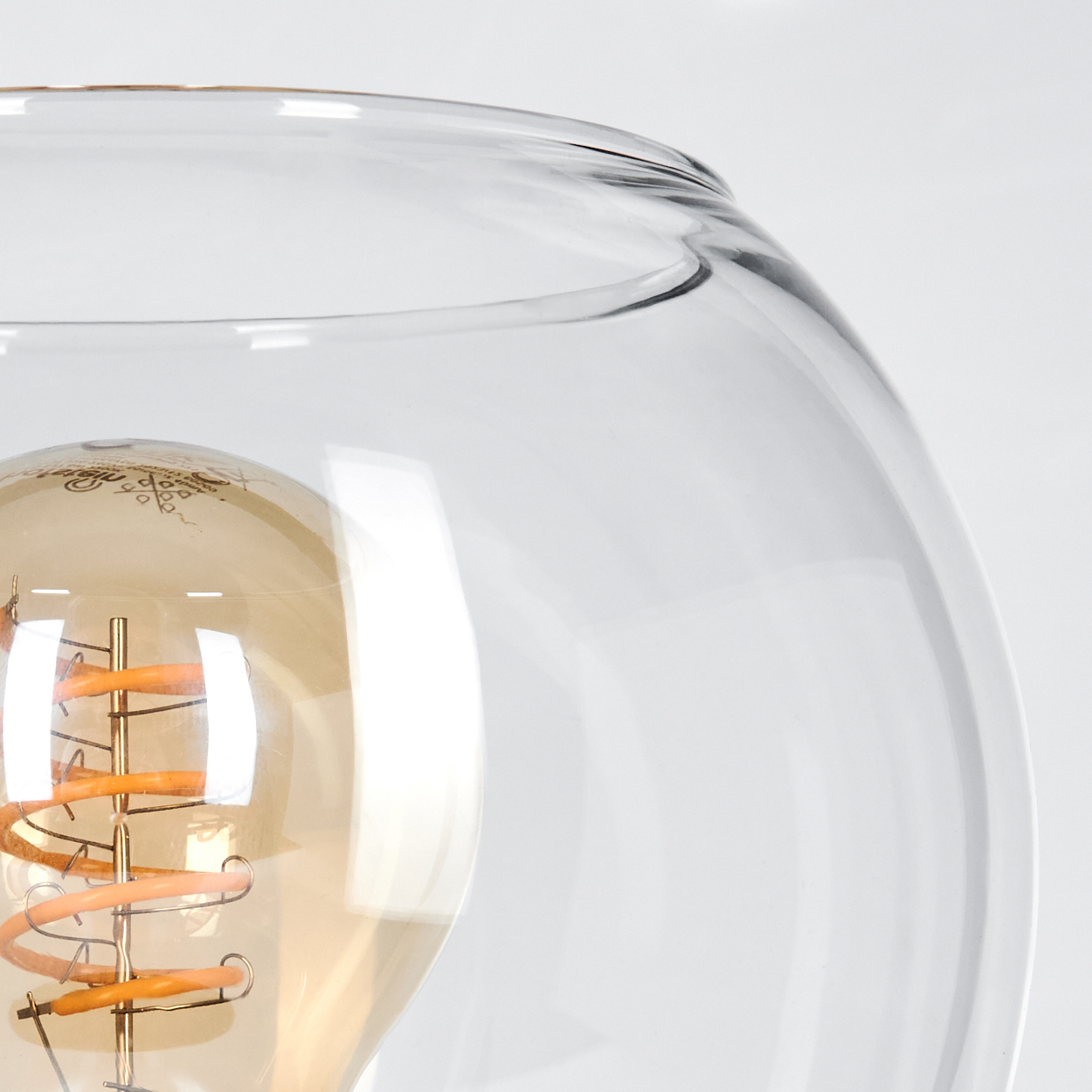 Nahaufnahme eines Glaslampenschirms mit sichtbarer Glühbirne. Die Glühbirne hat einen Spiralglühfaden und eine warme, goldene Farbe.