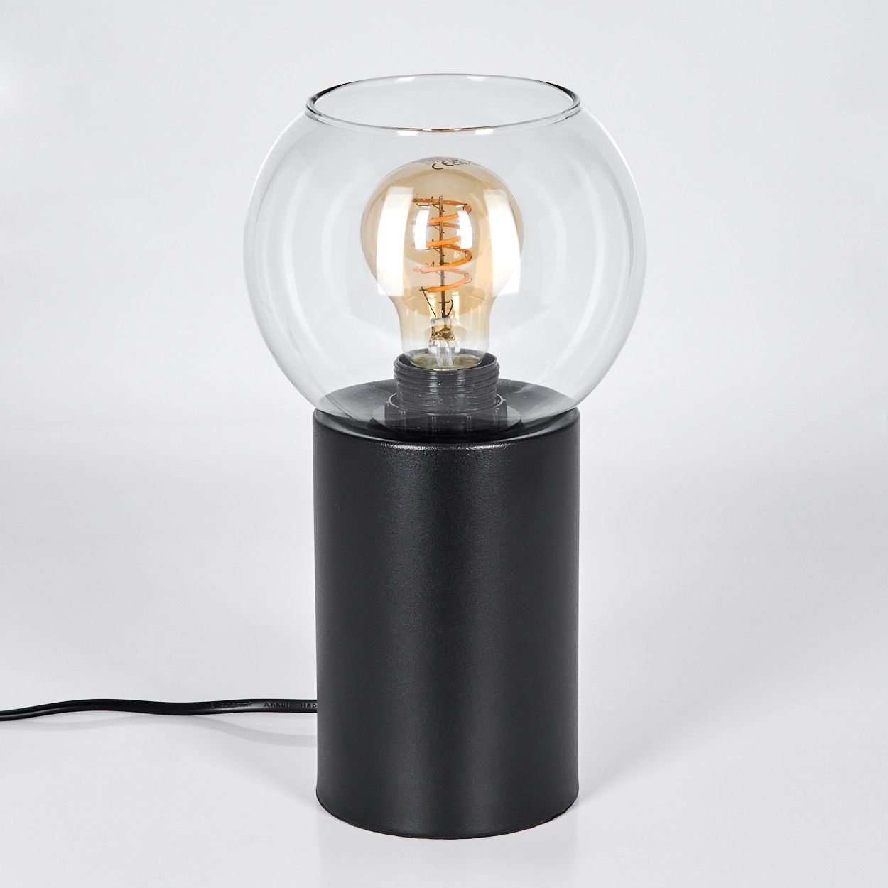 Eine moderne schwarze Lampe mit kugelförmigem Glasschirm, der eine sichtbare Glühbirne enthält, steht auf einer weißen Oberfläche.