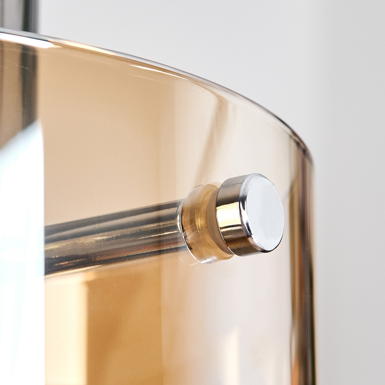 Nahaufnahme eines Glasschirmes mit Metallstange. Das Glas ist bernsteinfarben, das Metall hat Silber- und Chromdetails. Weißer Hintergrund.