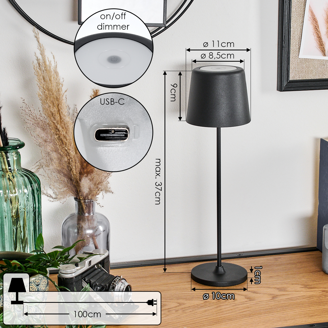 Eine schwarze Tischlampe mit Lampenschirm, USB-C-Anschluss und Ein/Aus-Dimmer. Sie steht auf einer Holzoberfläche mit Vase und Kamera.