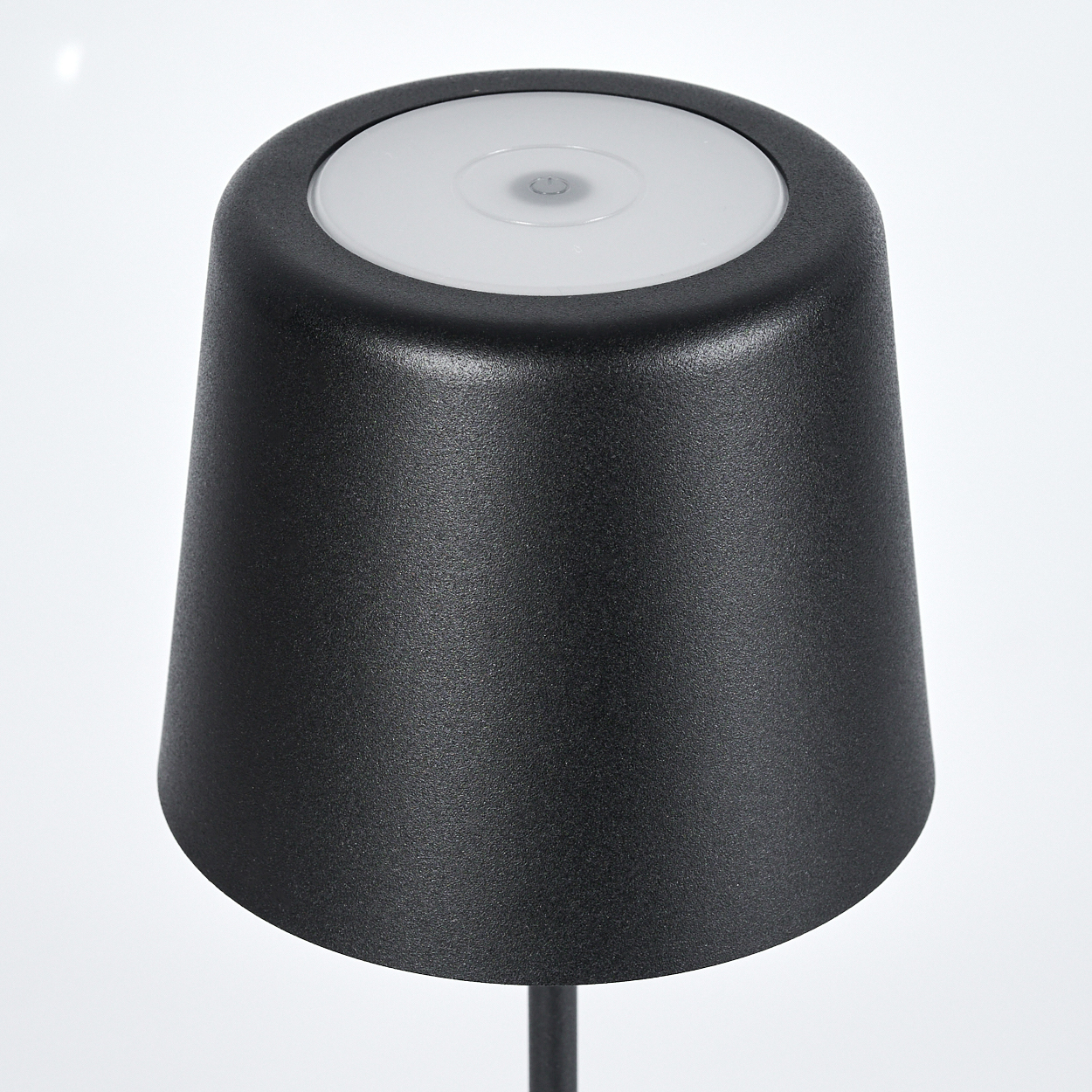 Eine schwarze Lampe mit weißer Oberseite auf weißem Hintergrund. Die Lampe ist kegelförmig.