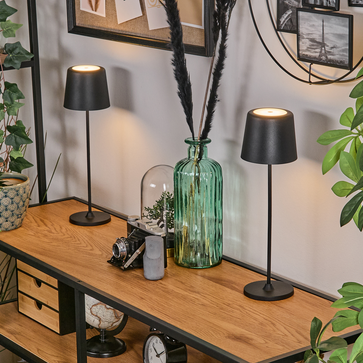 Zwei schwarze Lampen auf einem Holzregal mit dekorativen Gegenständen wie Globus, Uhr und grüner Glasvase mit schwarzen Federn.