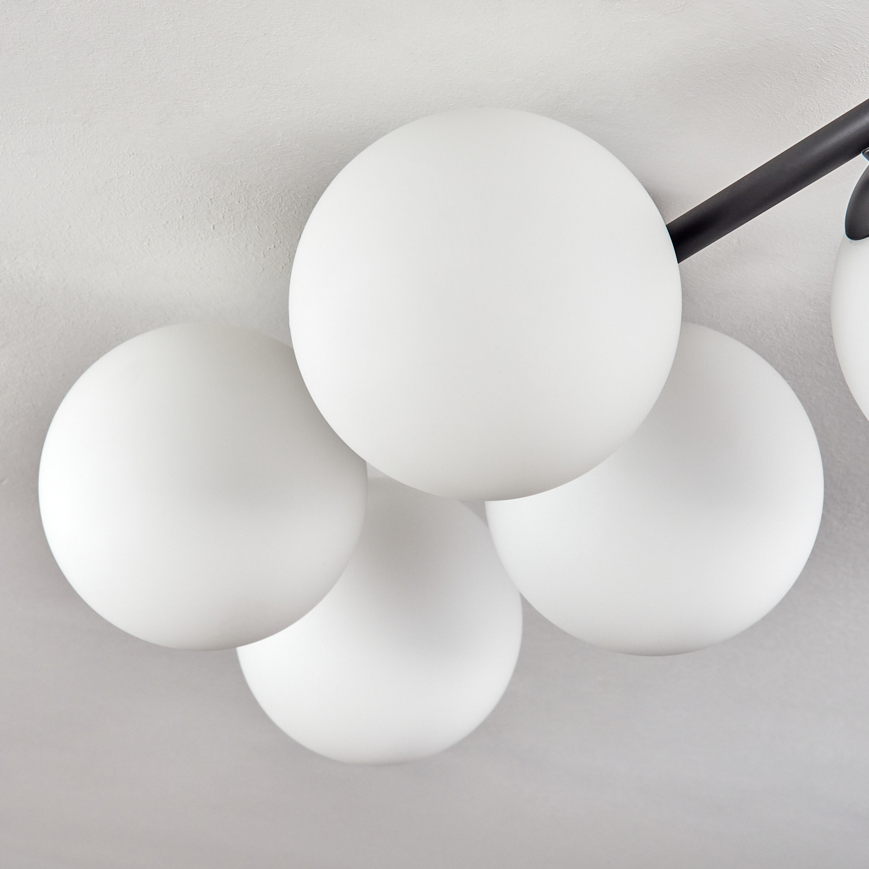 Nahaufnahme einer modernen Leuchte mit weißen Kugellampen. Die Lampen sind vor einem hellgrauen Hintergrund angeordnet.