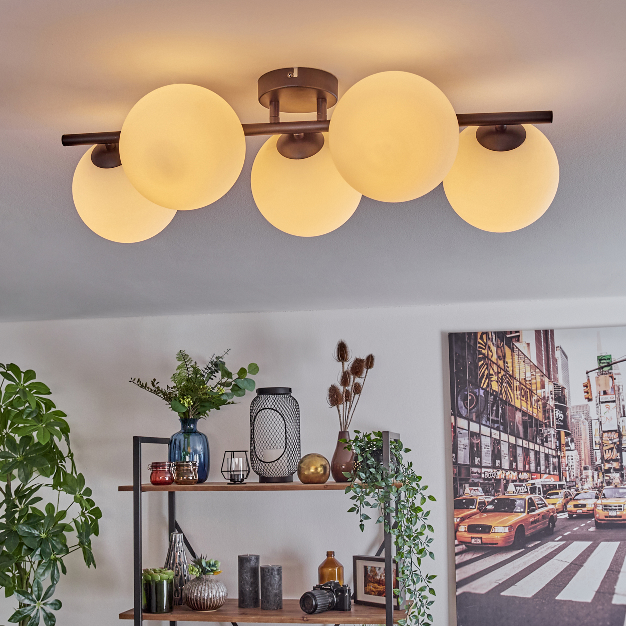 Eine moderne Deckenleuchte mit fünf kugelförmigen Lampen. Darunter ein Regal mit Dekoration und Pflanzen sowie ein Stadtbild.