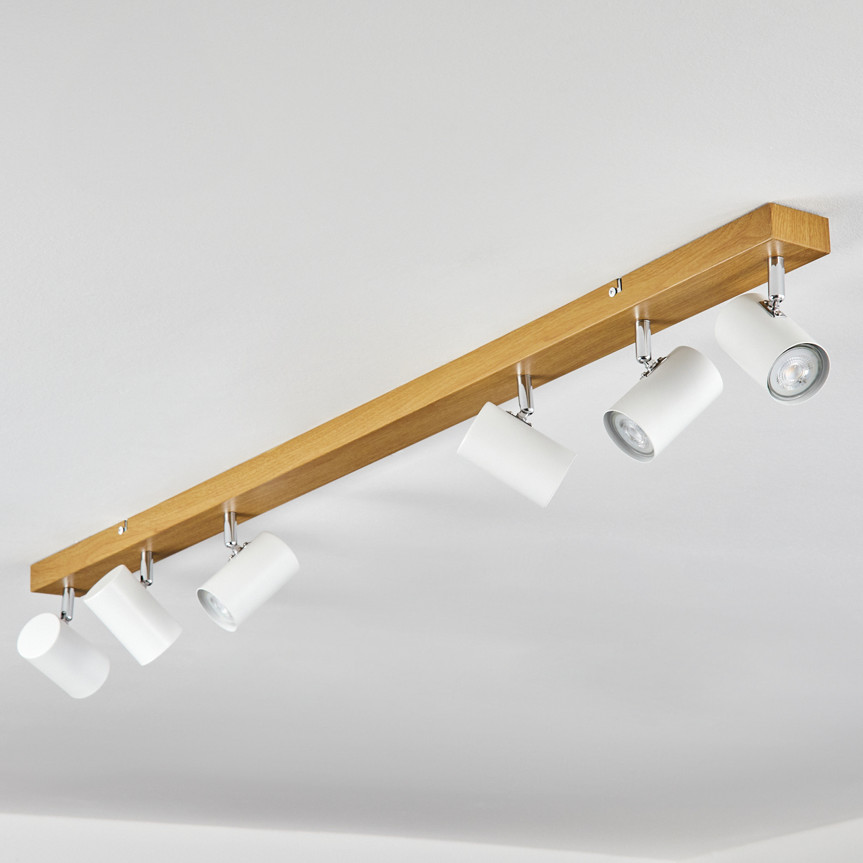 Ein Holzbalken mit sechs weißen Strahlern. Die Lichter sind nach unten gerichtet. Der Hintergrund ist eine schlichte weiße Decke.