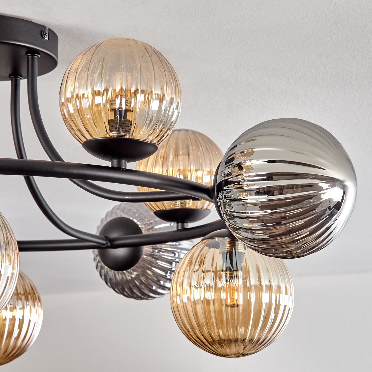 Eine moderne Deckenlampe mit mehreren kugelförmigen Glasschirmen in Bernstein und Silber, befestigt an schwarzen Metallarmen, vor einer weißen Decke.