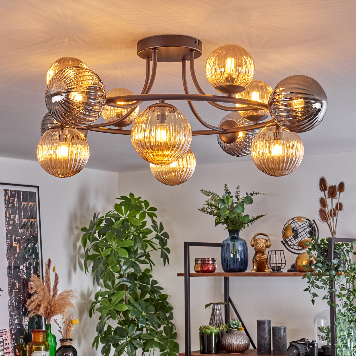 Eine moderne Deckenleuchte mit mehreren glühenden Glaskugeln hängt von der Decke. Darunter ein Regal mit Dekoration und Pflanzen.