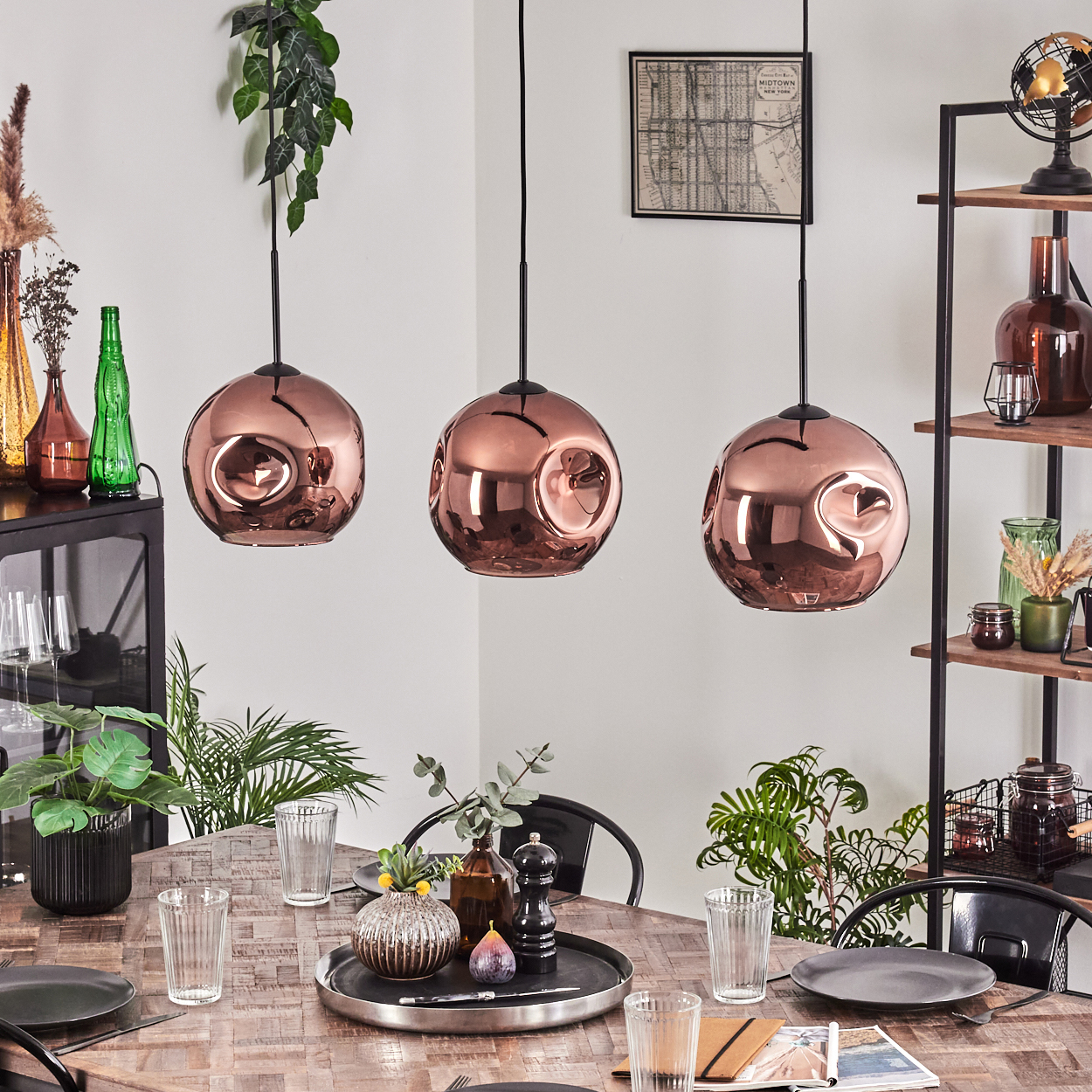 Esszimmer mit kupferfarbenen Pendelleuchten. Tisch mit Tellern, Gläsern und Dekoration. Regale mit Gegenständen. Pflanzen in Töpfen und hängend.
