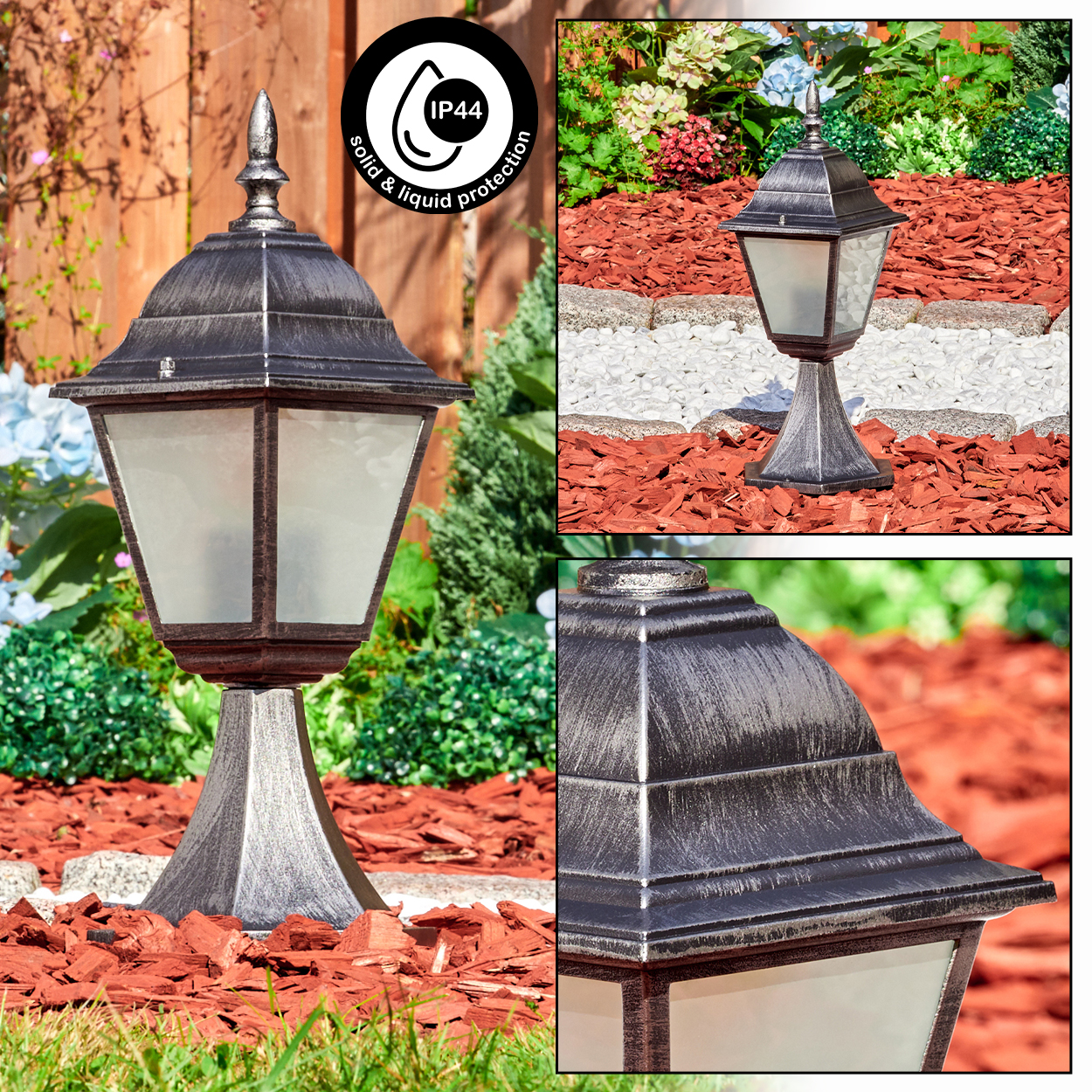 Eine metallische, verzierte Außenlampe steht in einem Garten mit roter Mulch. Die Lampe ist schwarz und silber mit Milchglas.