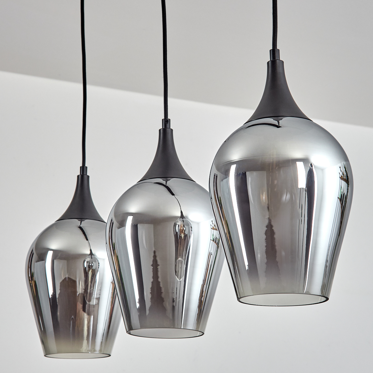 Drei silberne Pendelleuchten hängen von der Decke. Jede hat einen dunkelgrauen Aufsatz und einen reflektierenden Glasboden.