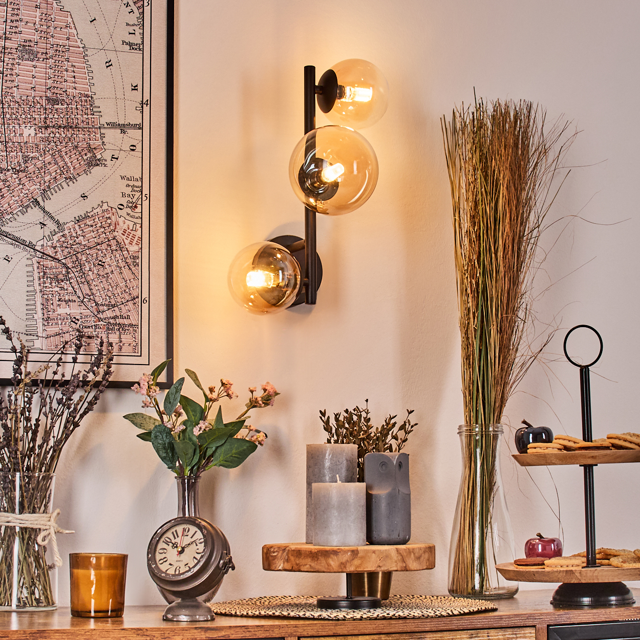 Ein Raum mit Wandlampe, Karte, Blumen, Kerzen und Dekorationsartikeln auf einer Holzoberfläche. Ein zweistöckiges Tablett mit Keksen.
