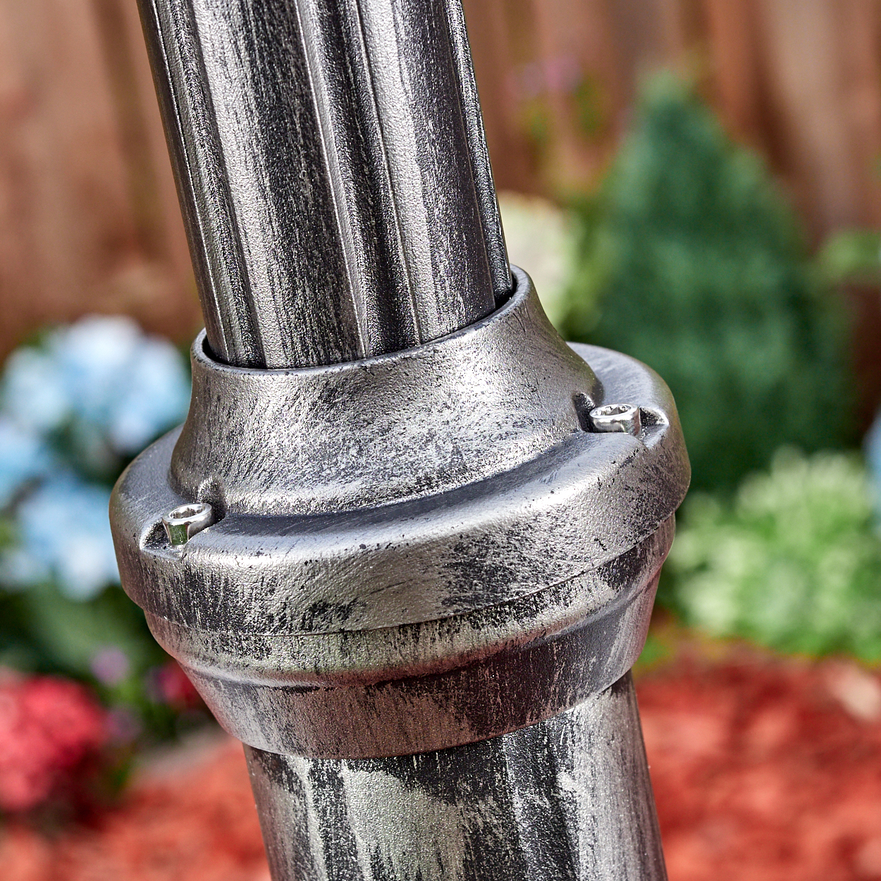 Nahaufnahme einer silbernen Metallstange mit gerilltem Design und einer Verbindungsbasis, mit unscharfem Gartenhintergrund.