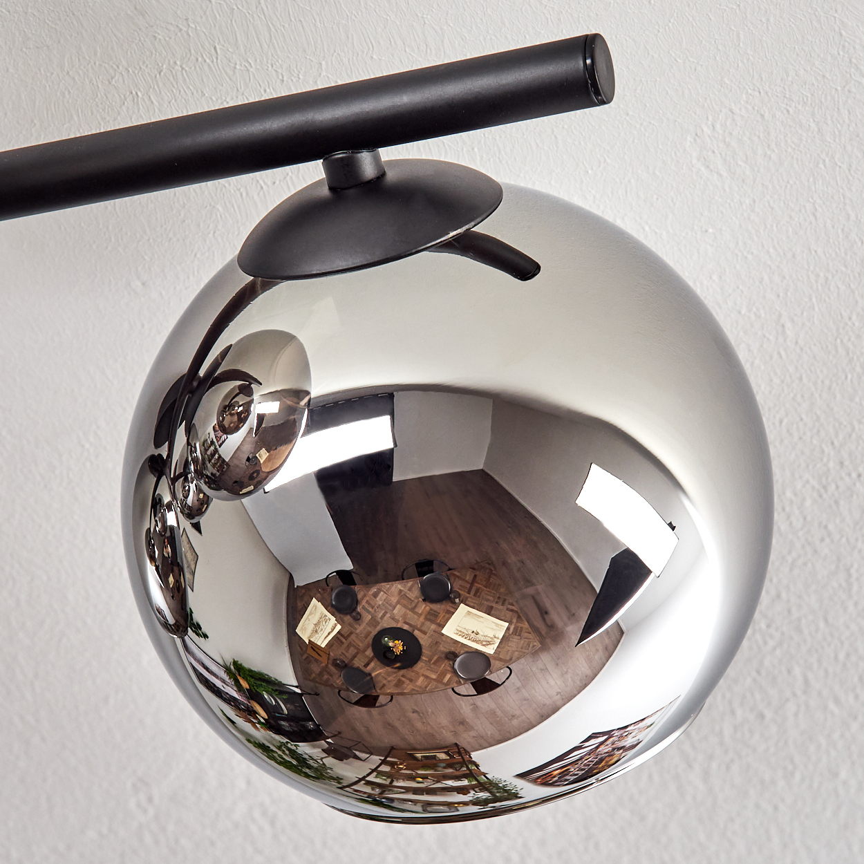 Eine reflektierende Kugelleuchte. Die Kugel reflektiert einen Esstisch und Stühle an einer weißen, strukturierten Wand.